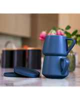 Two navy blue ceramic mugs stacked on a kitchen counter with blurred background