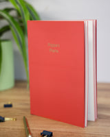 Red notebook with 'Pippa's Plans' on a wooden surface with a plant in the background