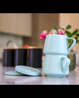 Two light blue mugs stacked on a kitchen counter with blurred background